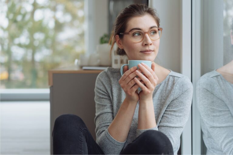Serious young woman sitting daydreaming with mug of coffee